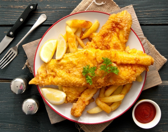 Fish filet's and french fries on a plate with cutlery and napkins