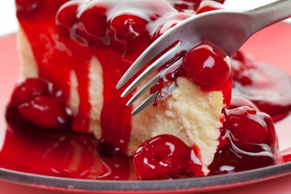 A fork slicing into a piece of cherry cheese cake