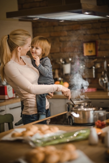 Happy mother talking to her small son while cooking meal in the kitchen. Focus is on boy.