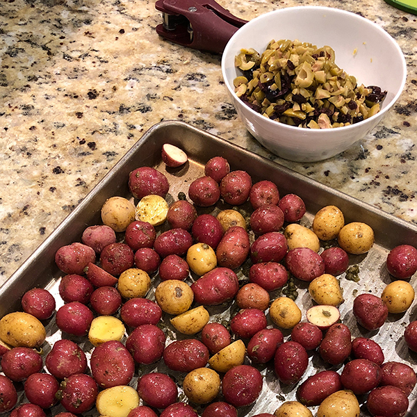 A pan of roasting potatoes next to a bowl of mixed ingredients. 